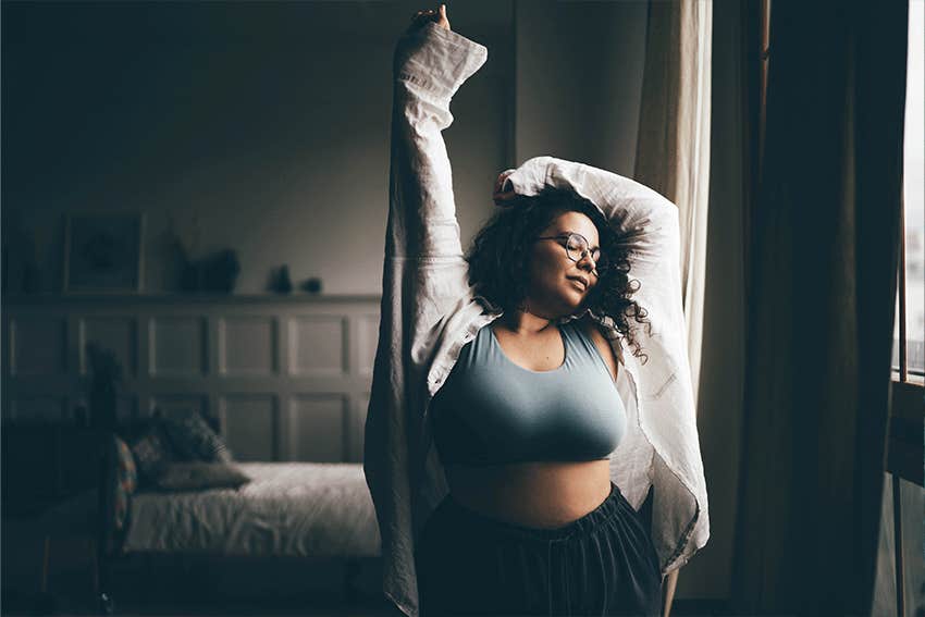 Curly haired plus size woman wearing comfortable clothes dances in stylish room.