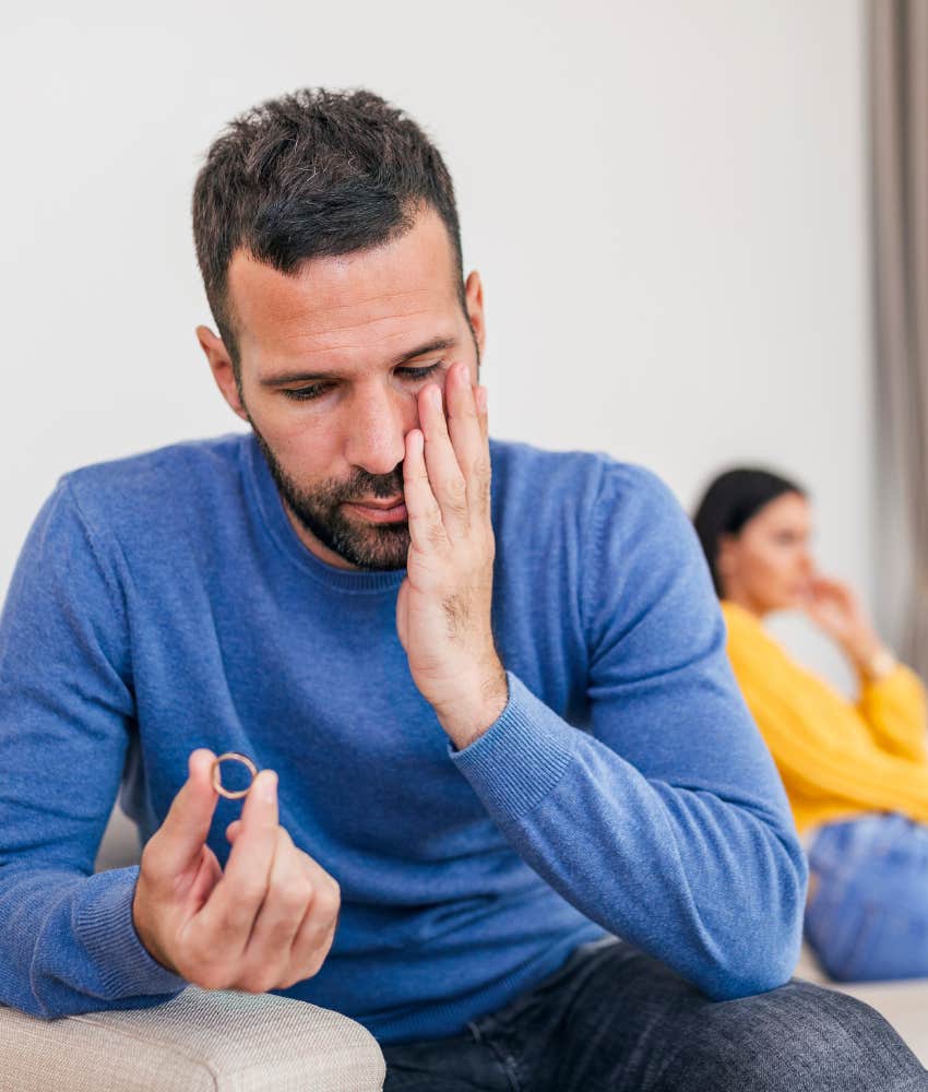 Man holding his wedding ring with wife sad in the background