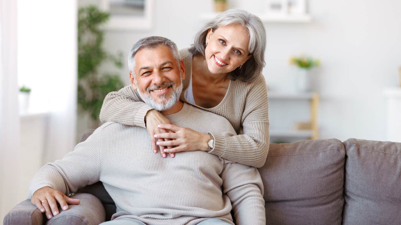 close up of smiling wife with arms around husband sitting on couch