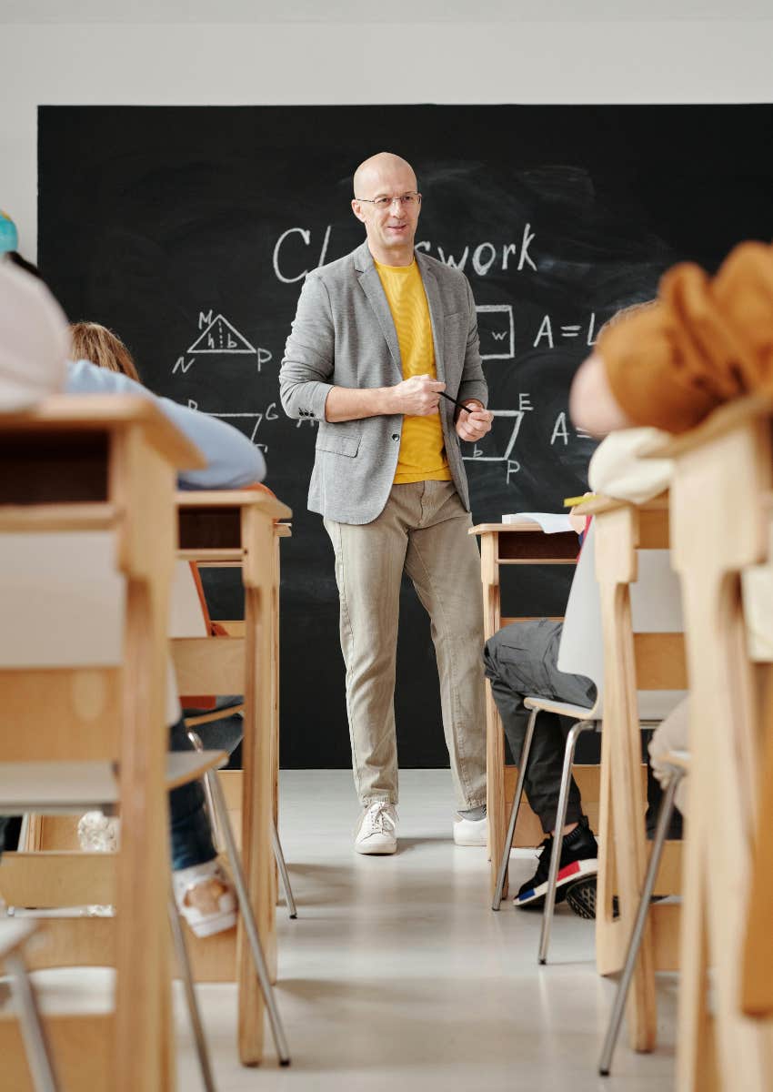 math teacher standing in front of classroom with board behind him