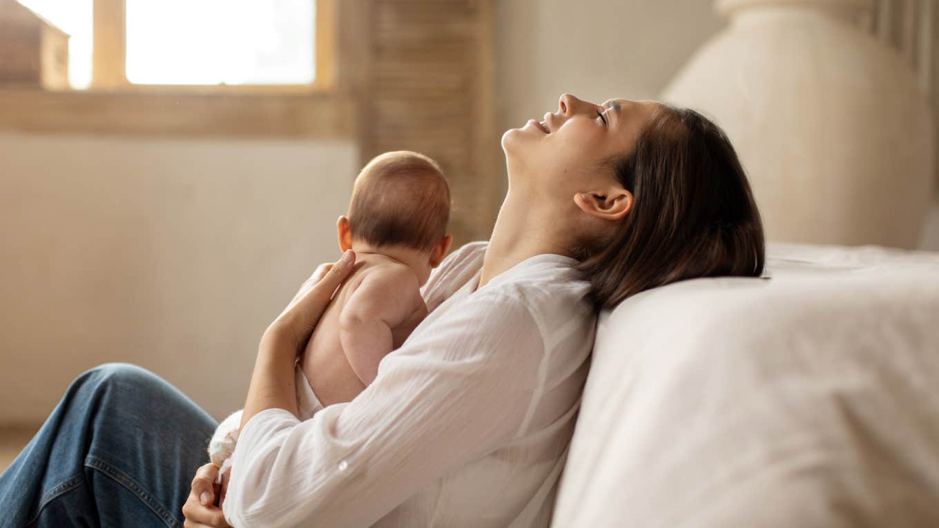 Tired young mother sitting on floor and holding newborn baby on hands