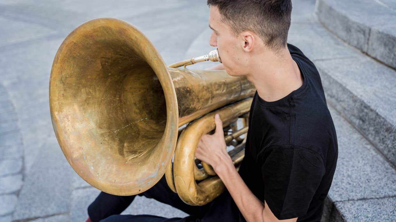 young man sitting on steps outside playing tuba