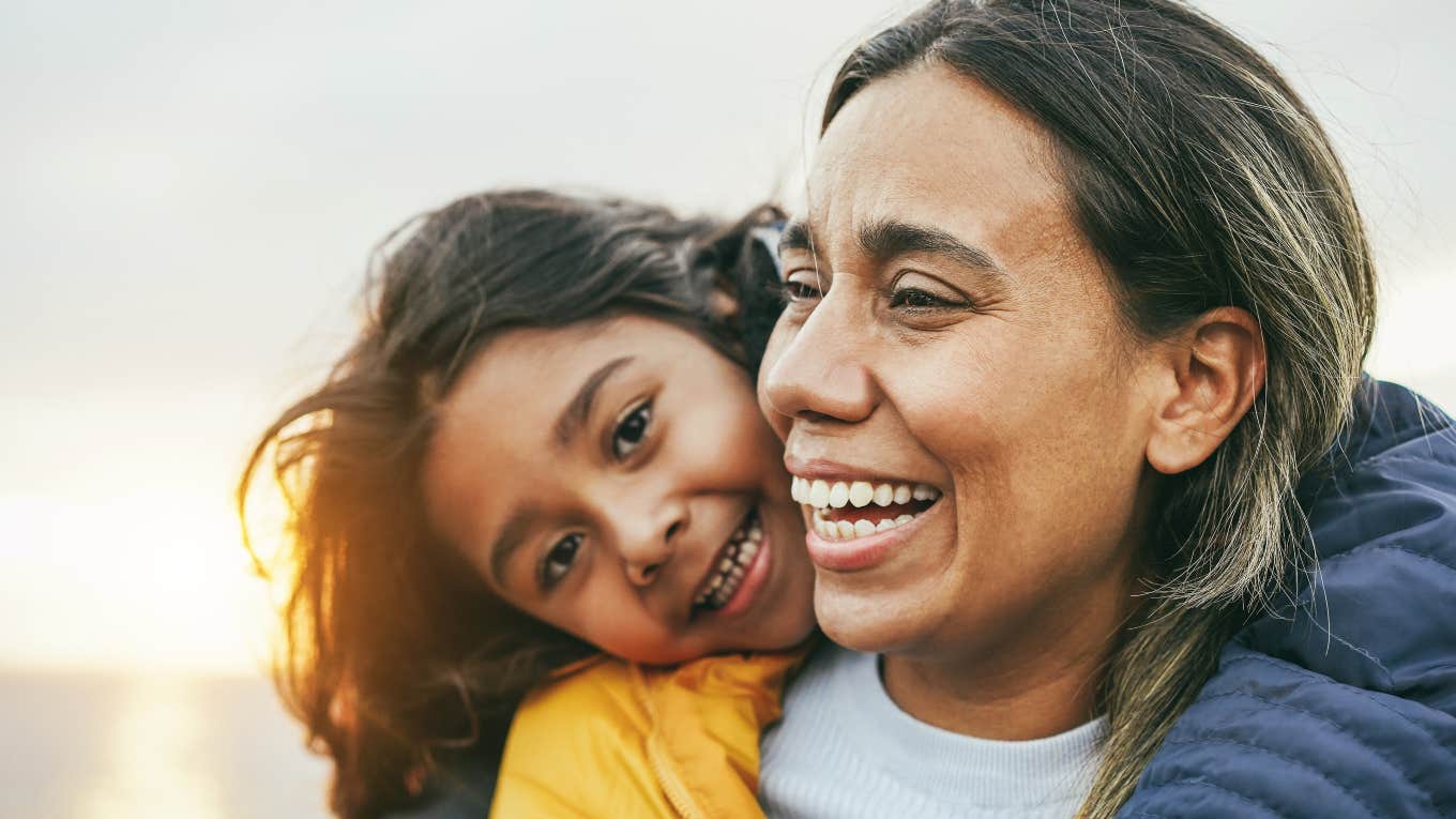 little girl with arms around her mother's shoulders from behind