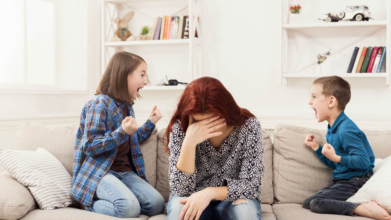 two kids fighting while tired, frustrated mom hangs her head between them