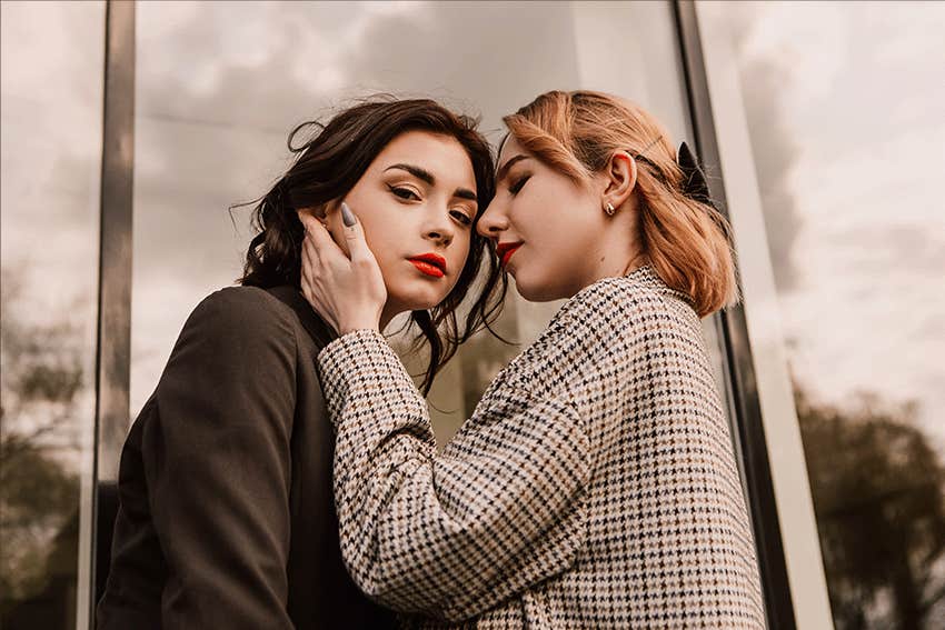 Two women posing near glass building. 