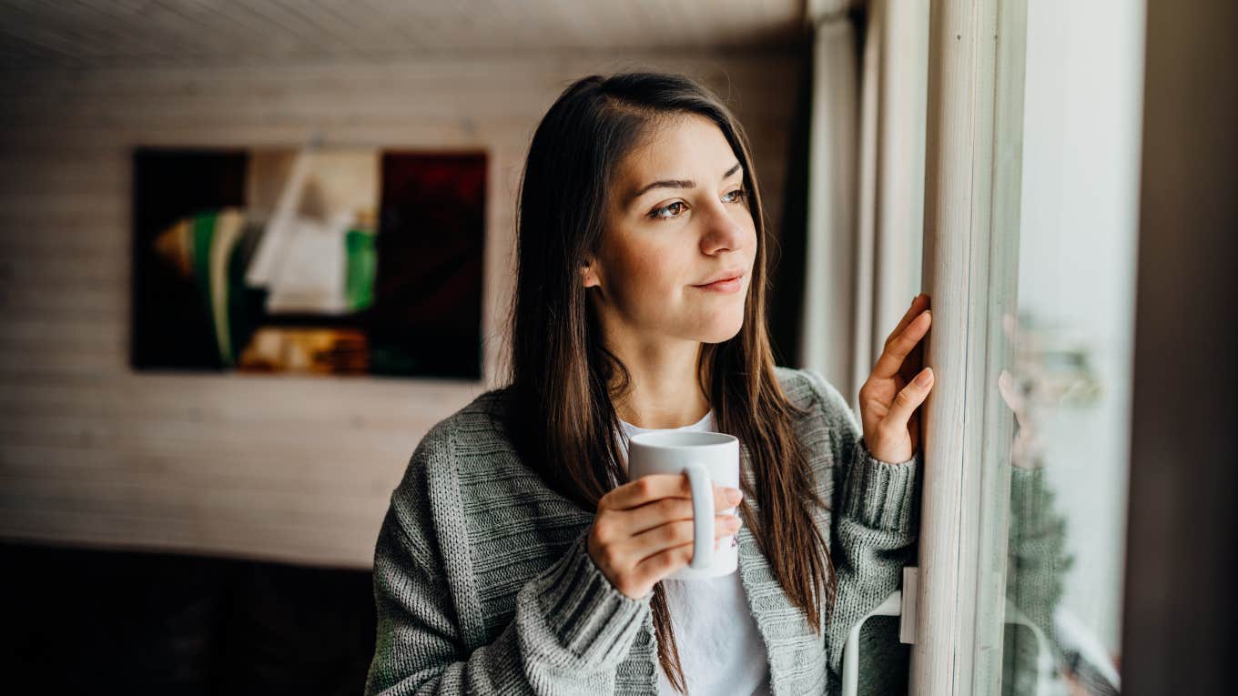 Woman looking out the window alone holding a cup of coffee