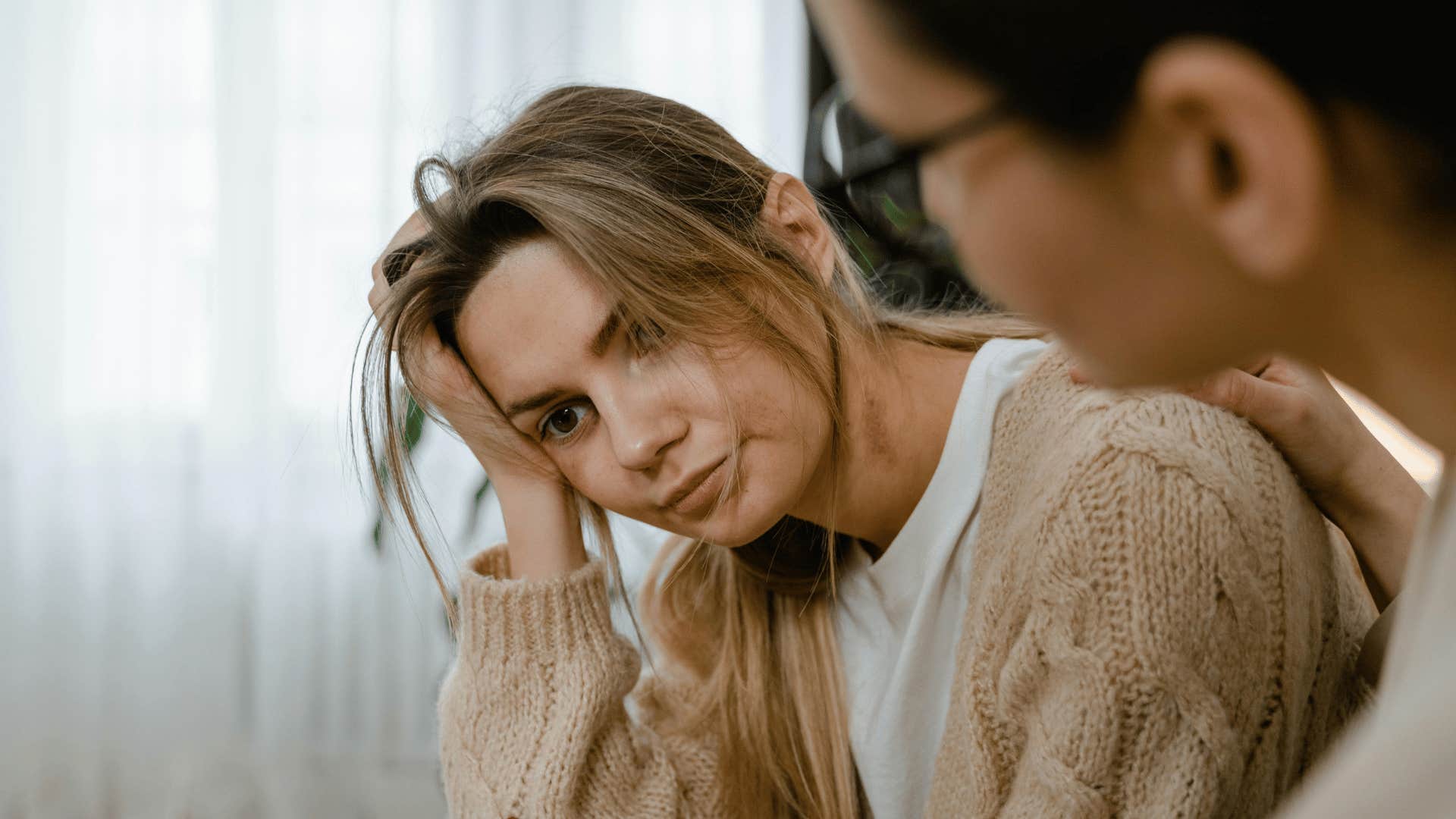 woman looking upset with hand in hands while friends tries comforting her