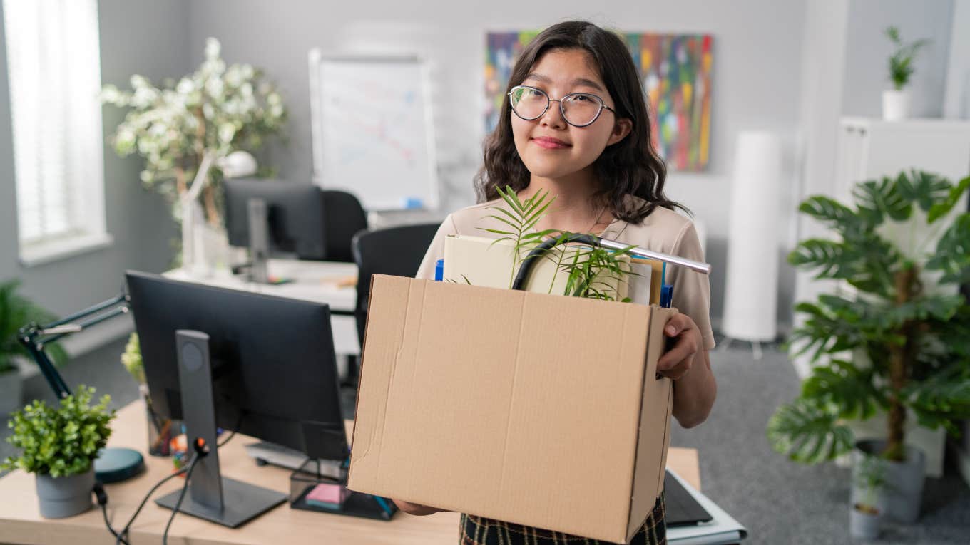 smiling woman walking out of office with box of things after quitting