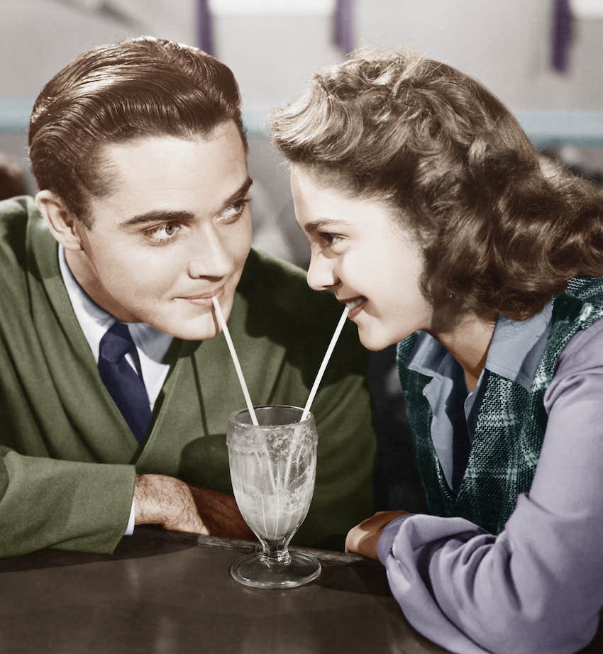 Vintage couple in love share and old-fashioned milkshake with 2 straws