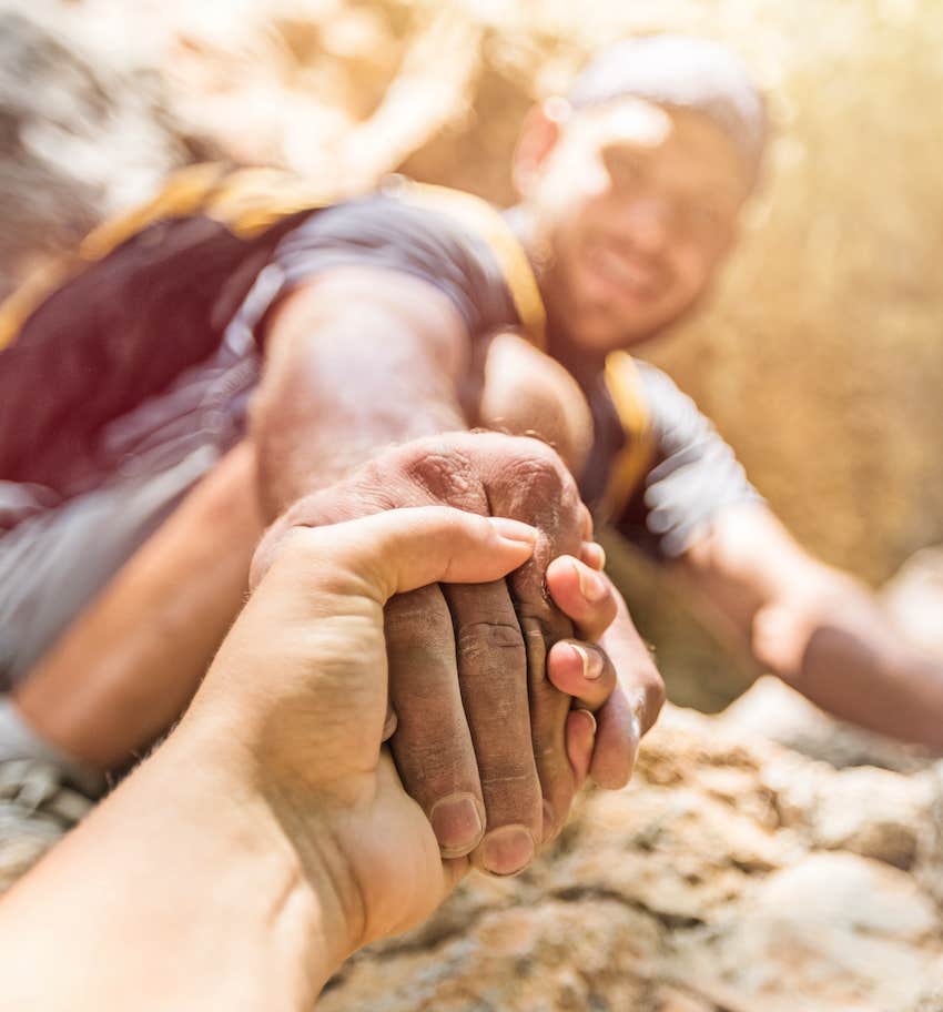 Climber reaches to give hand up and accept the challenge to attract happiness