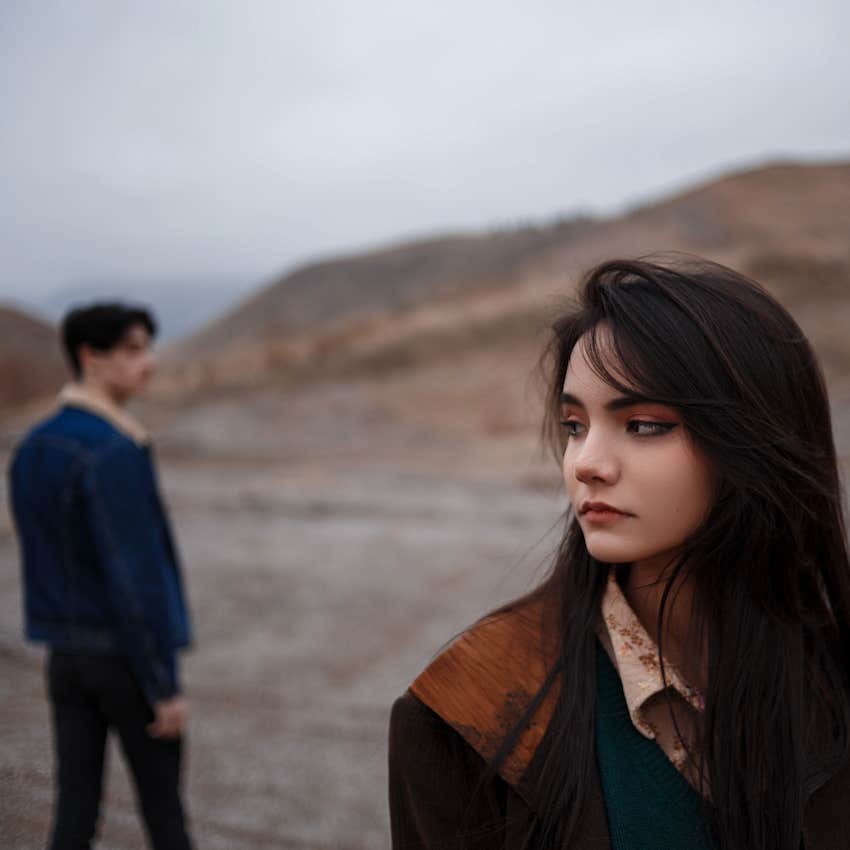 Man stand in distance behind woman, she believed he was in love, now she looks away