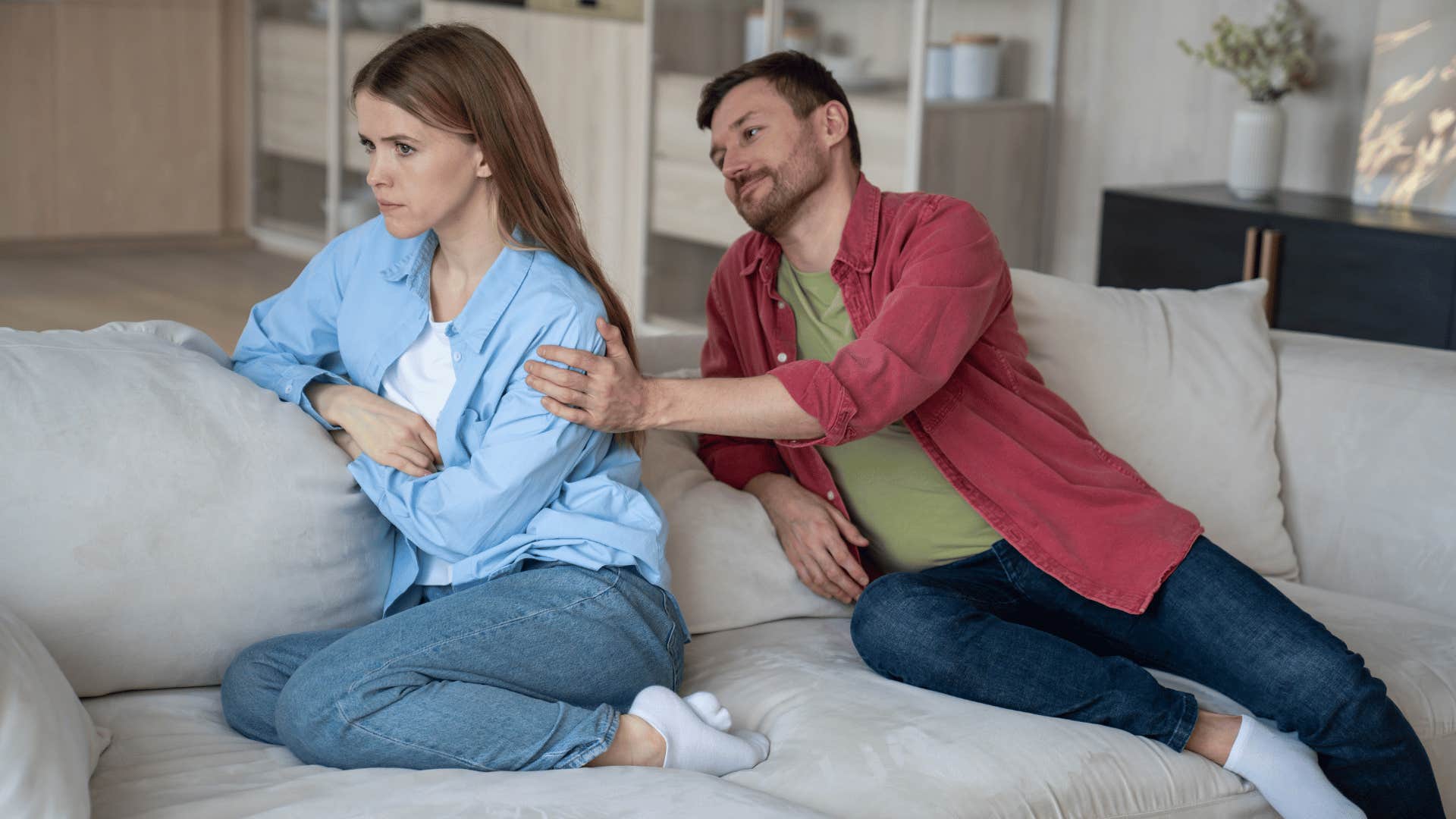 woman and man sitting on the couching while man tries to comfort woman