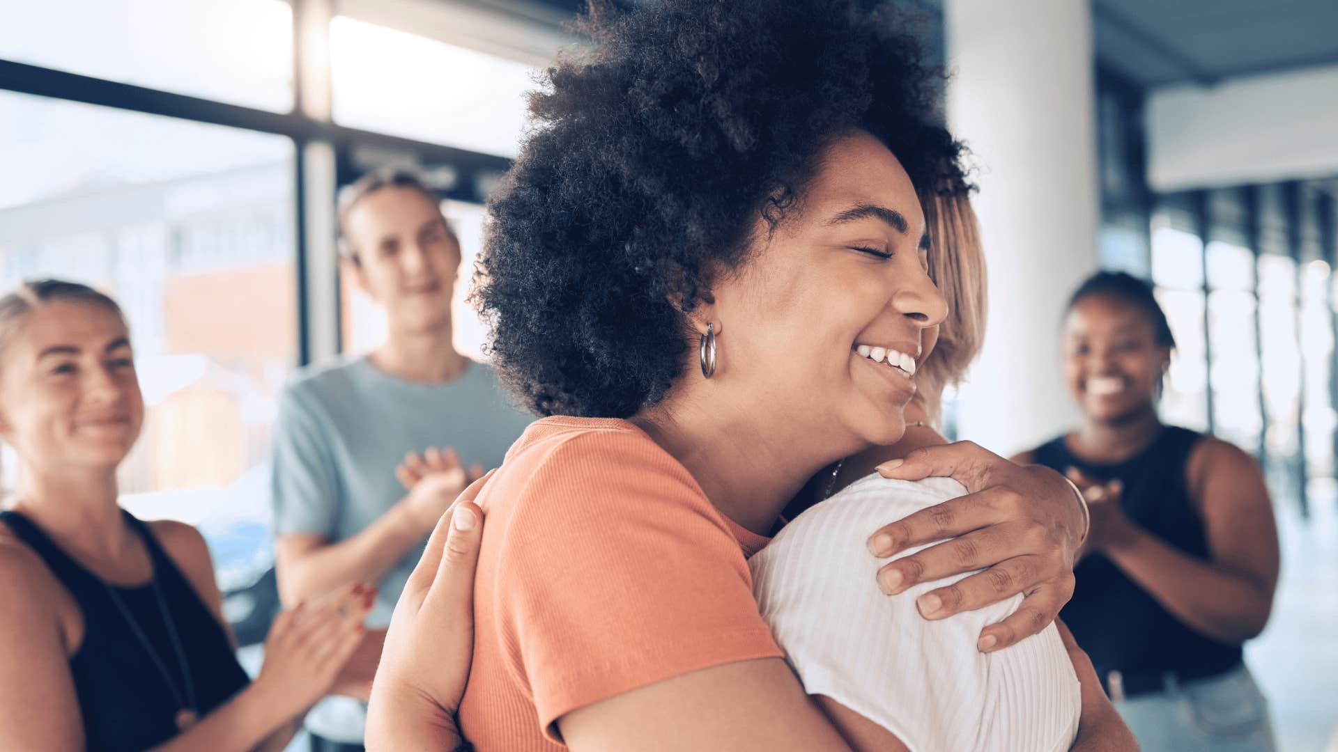 woman hugging other woman while other people clap and watch