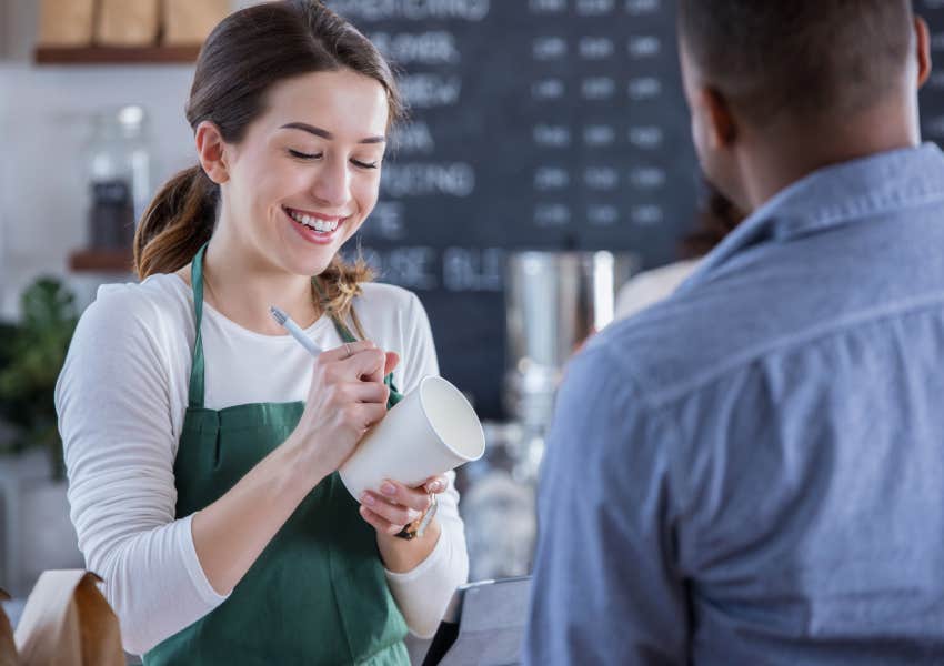 smiling barista writes order and note on a coffee togo cup for customer 