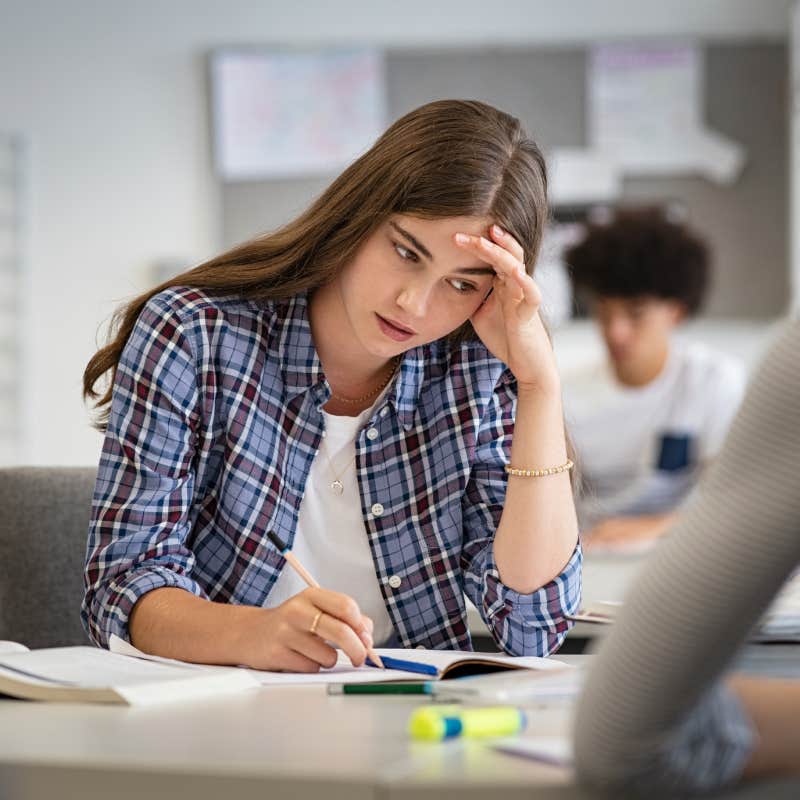 Anxious young woman with hand on head feeling tired while studying at school