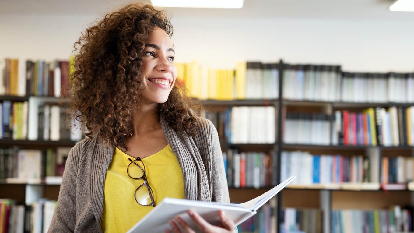 Smiling student girl reading book in library