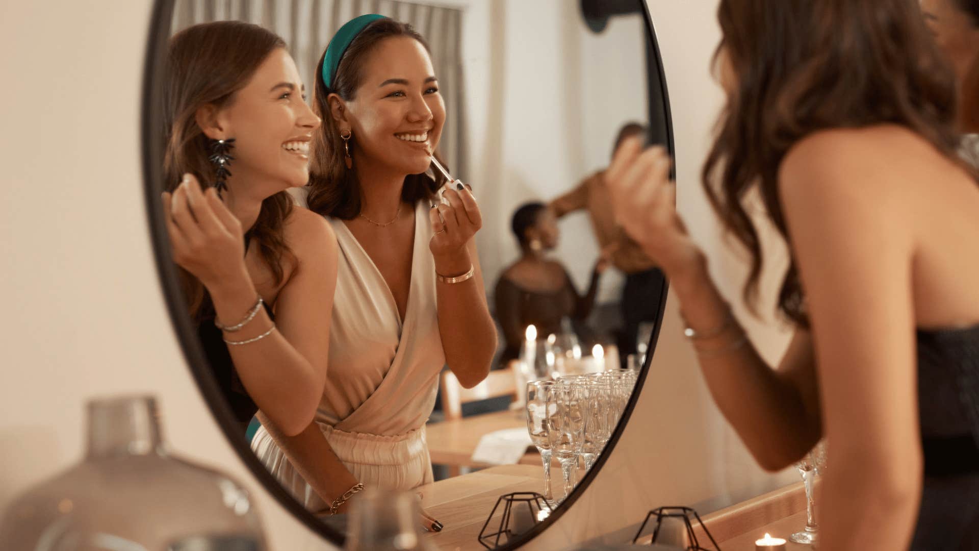 two women doing makeup in front of mirror and smiling 