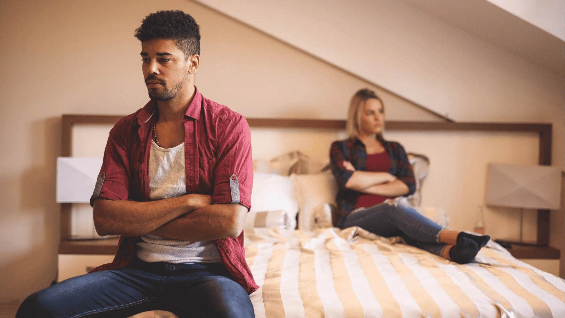 couple sitting on bed distant from each other and upset