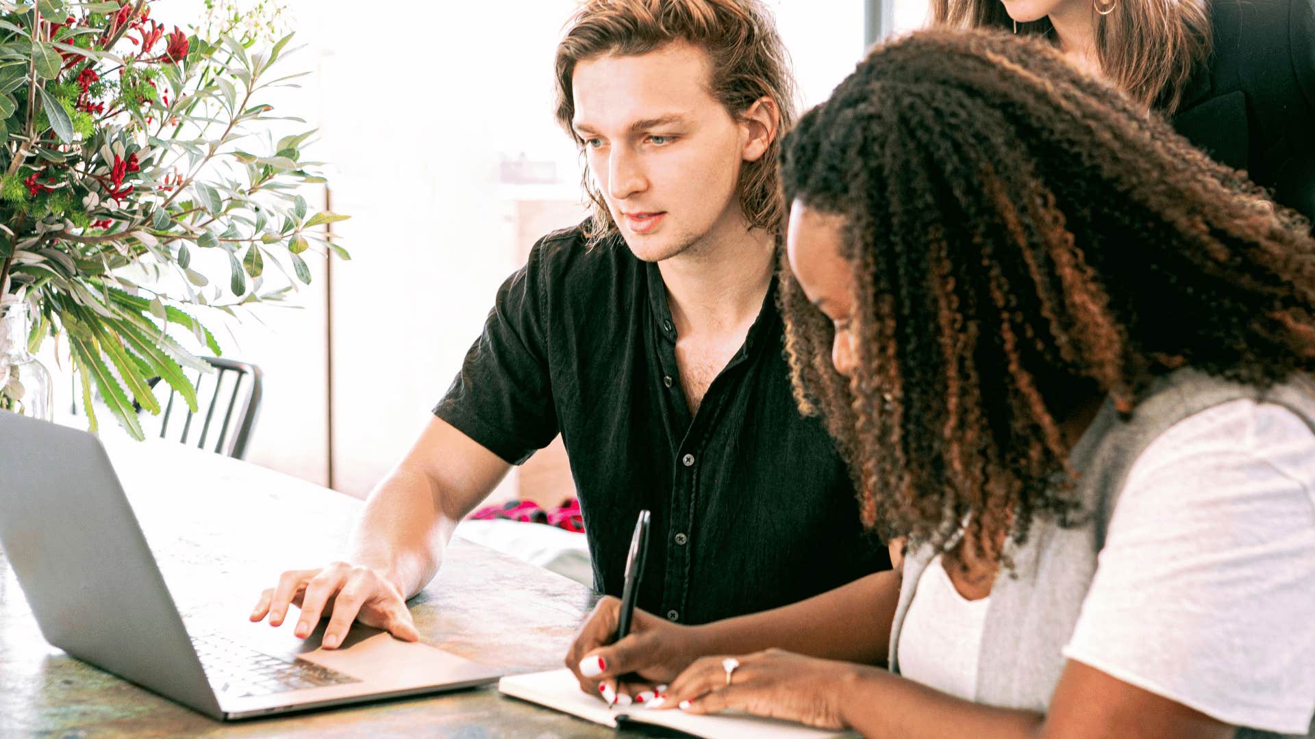 man and woman looking at laptop writing notes