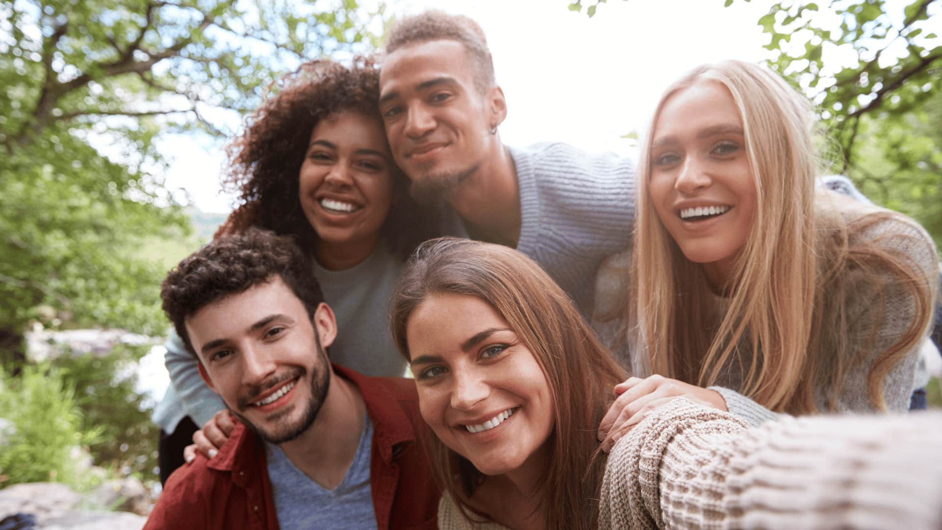 Group of five smiling friends pull in close for a photo