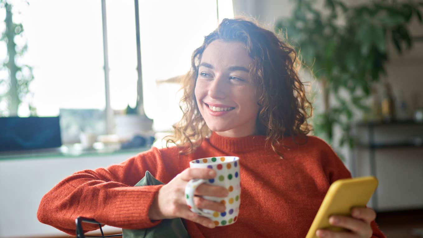 smiling woman holding a cup of coffee and phone