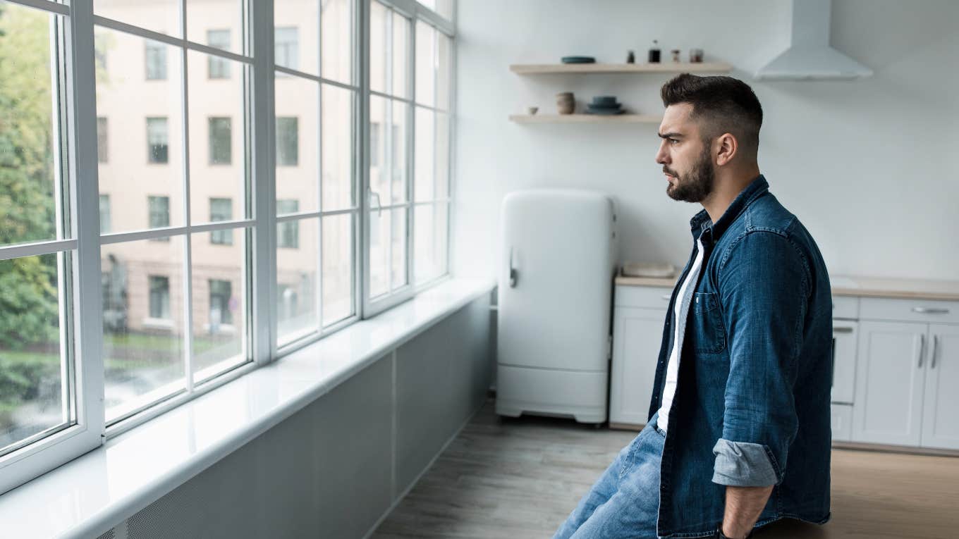 sad man leaning on kitchen table looking out the window