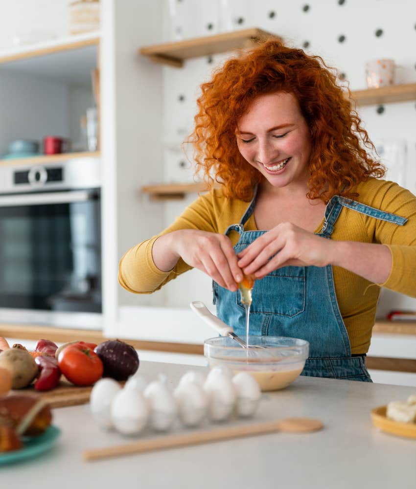 Woman with red hair happily cooking breakfast