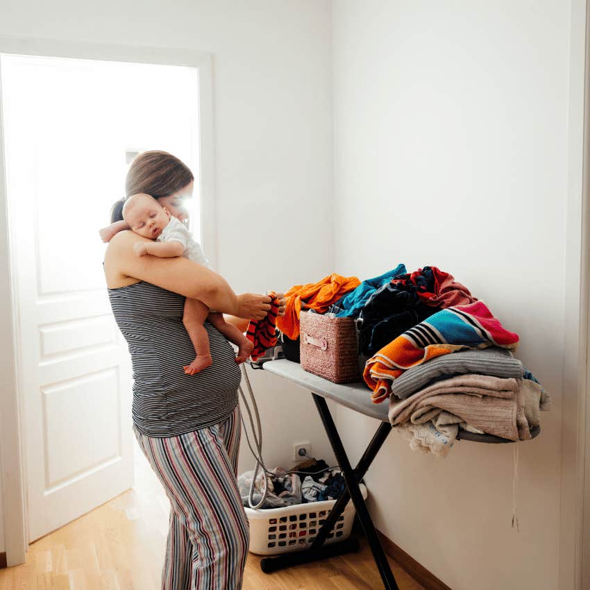 new mom holding baby while folding laundry