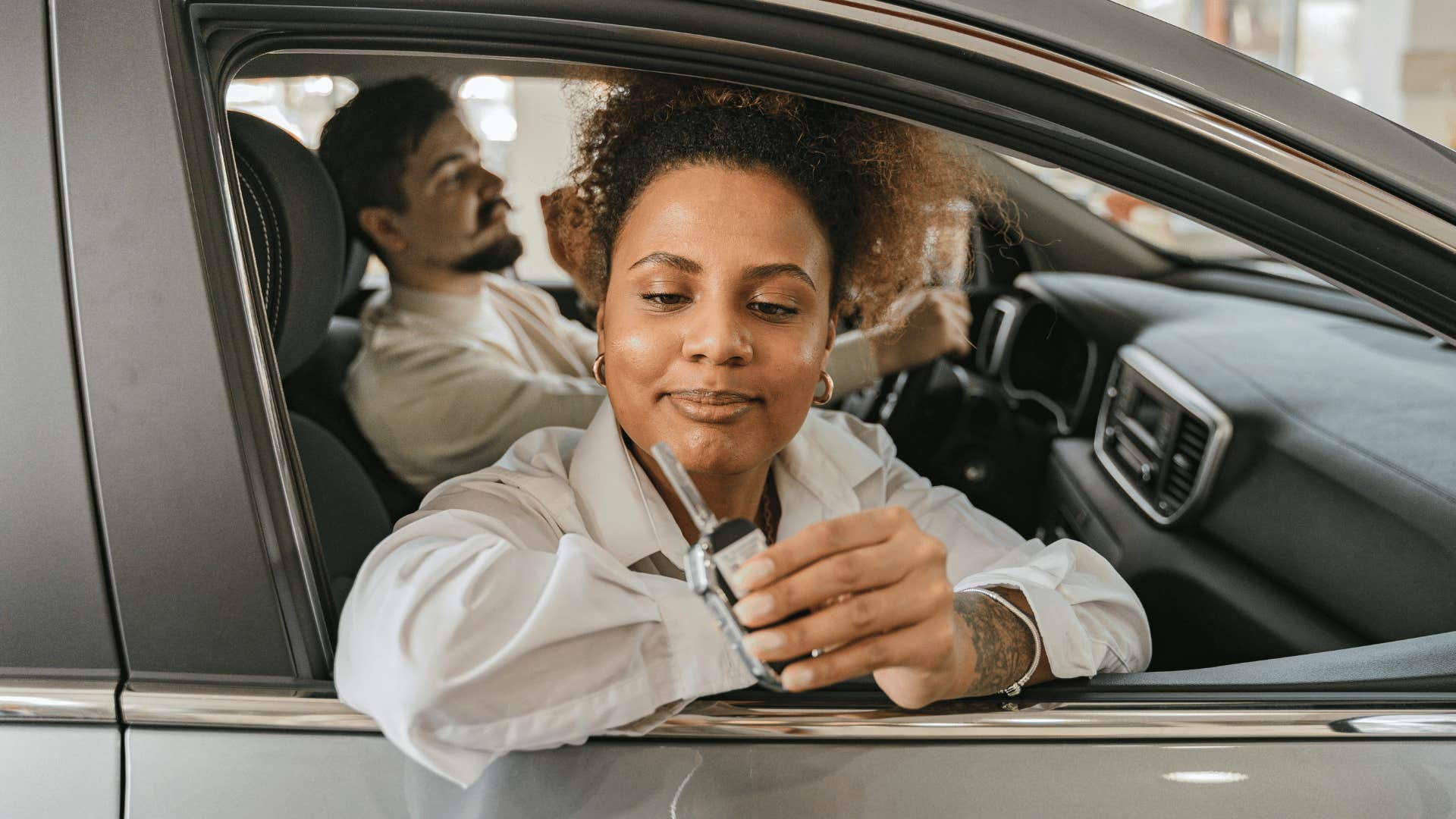 woman holding up key with man driving