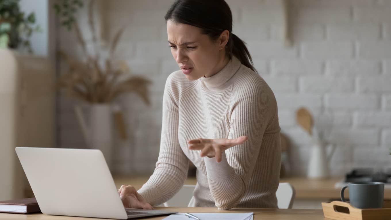 Irritated woman sit at table staring at laptop screen