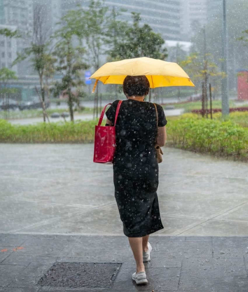 Woman leaving work in a rain storm with a yellow umbrella