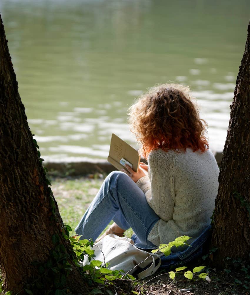 woman reading a book next to a river