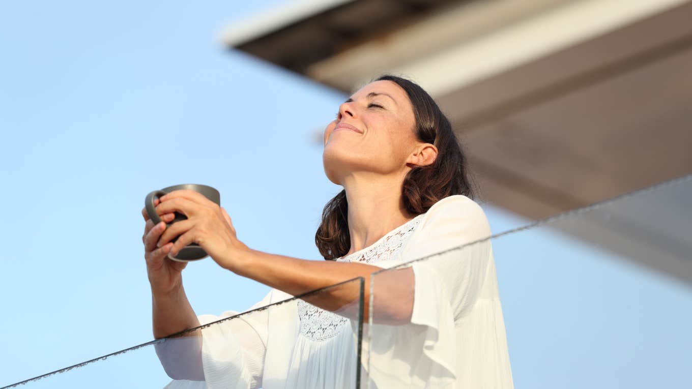 Woman smiling in the sun holding a cup of coffee