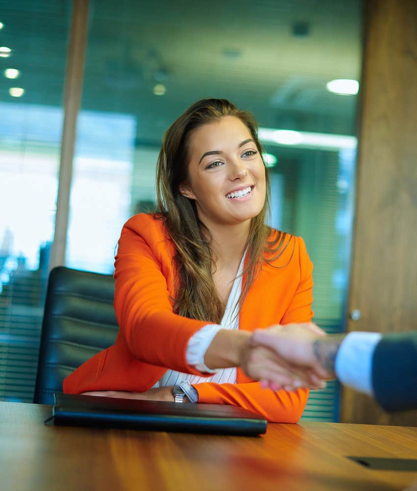 woman in orange blazer shaking hands at job interview