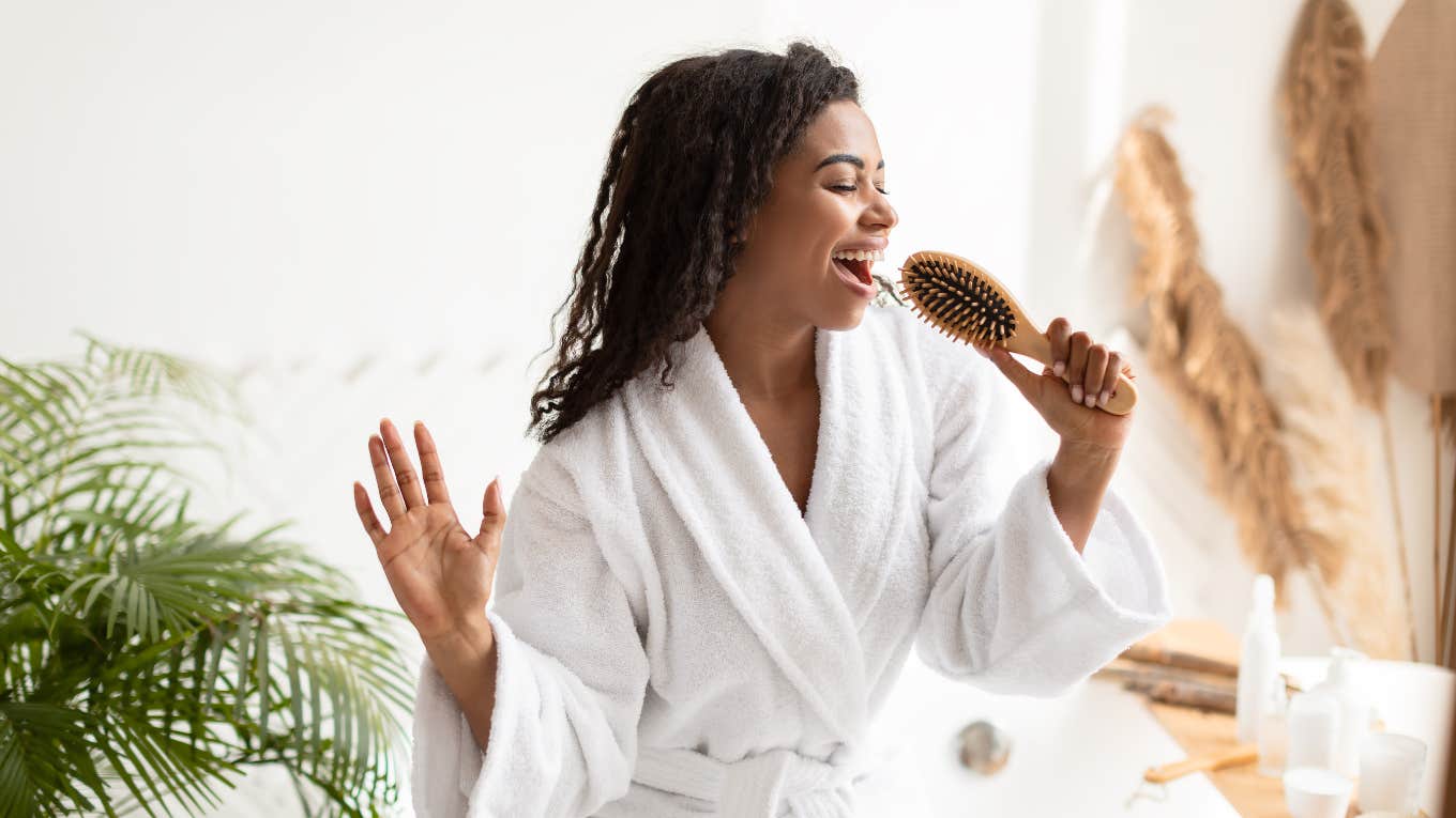 Freshly showered woman in a white robe singing into the handle of her hairbrush