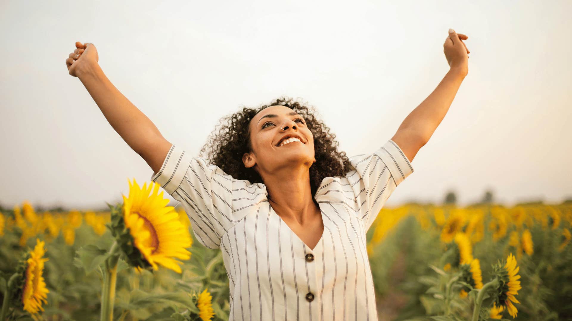 young woman with raised arms in sunflower field