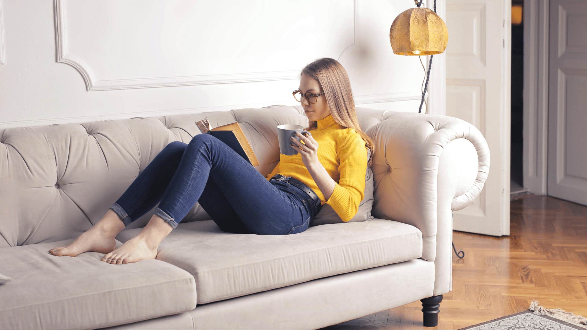 young woman reading on couch and holding a mug