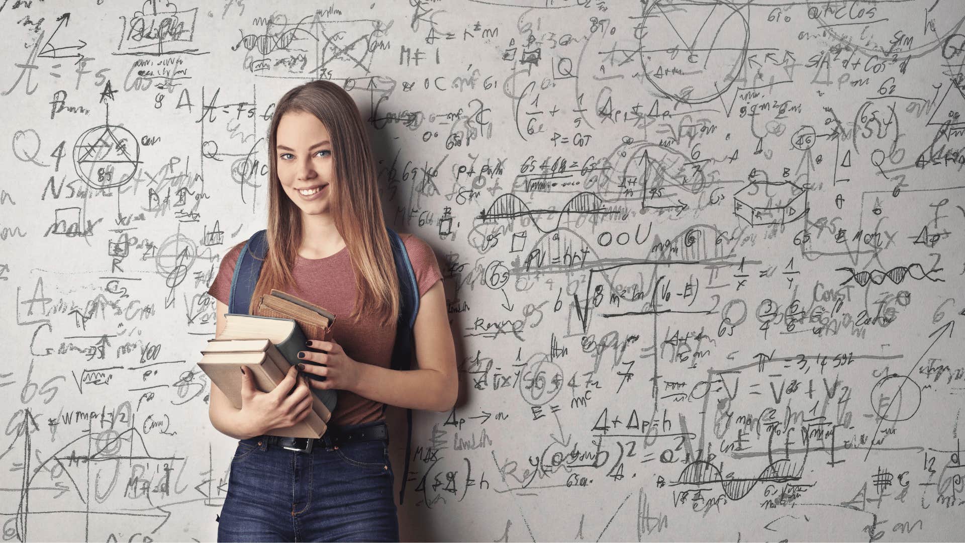 student holding books in front of board of math equations