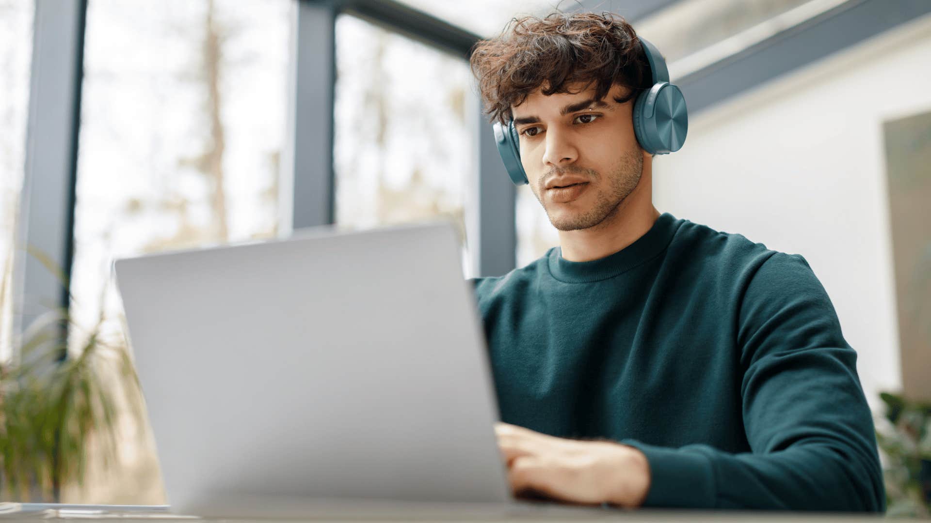 man wearing headphones focused on open laptop