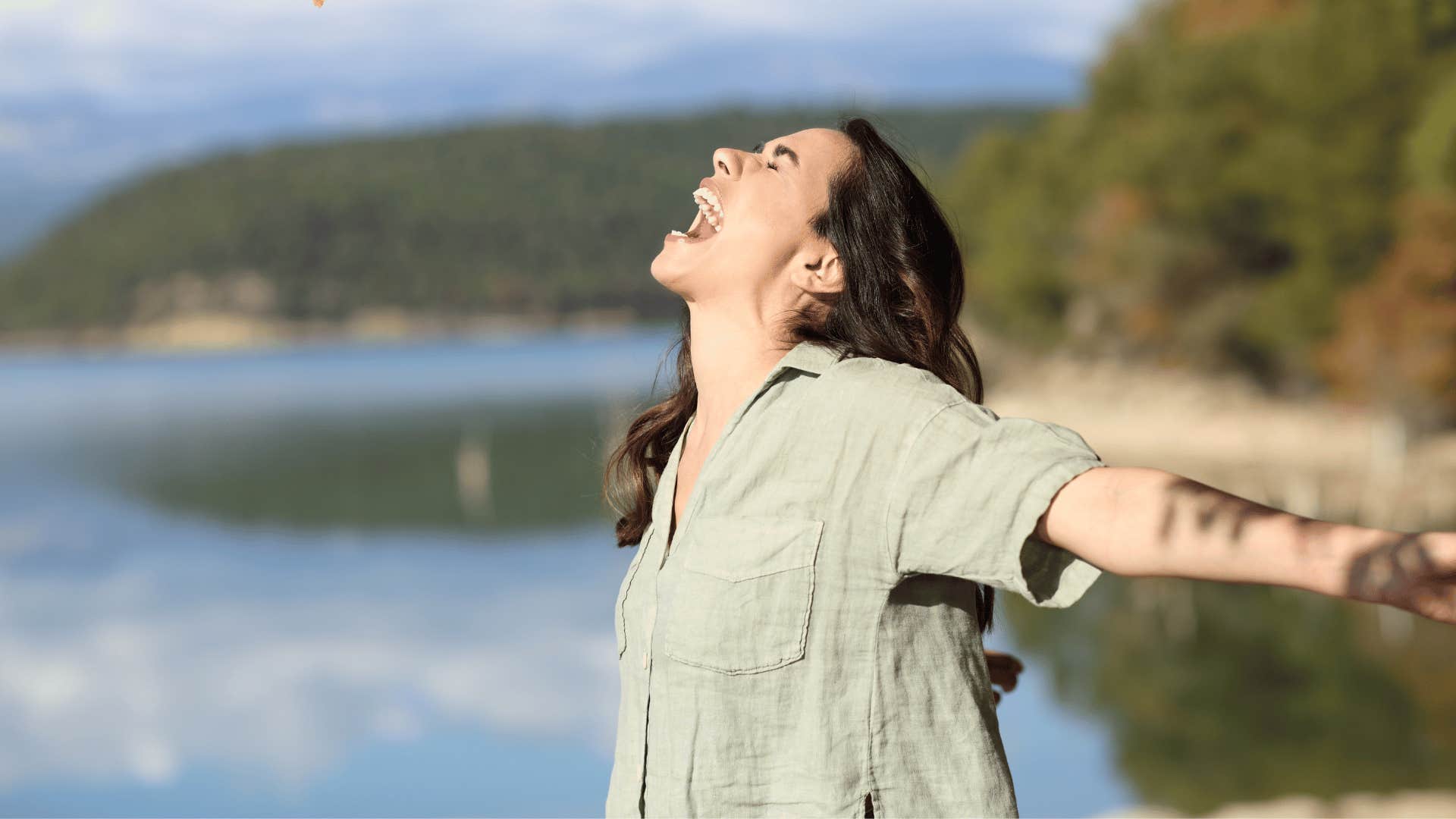 young woman with arms wide and screaming by lake