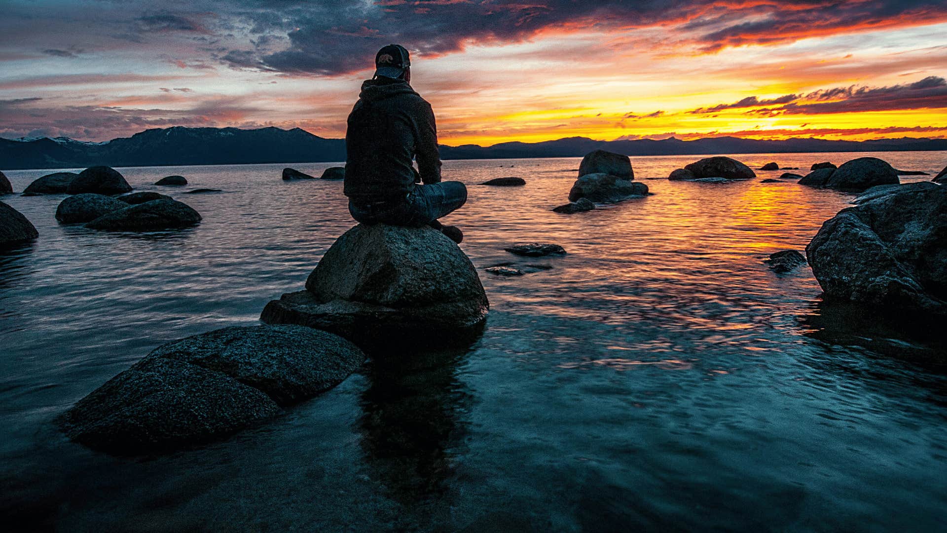 man sitting on rock watching sunset