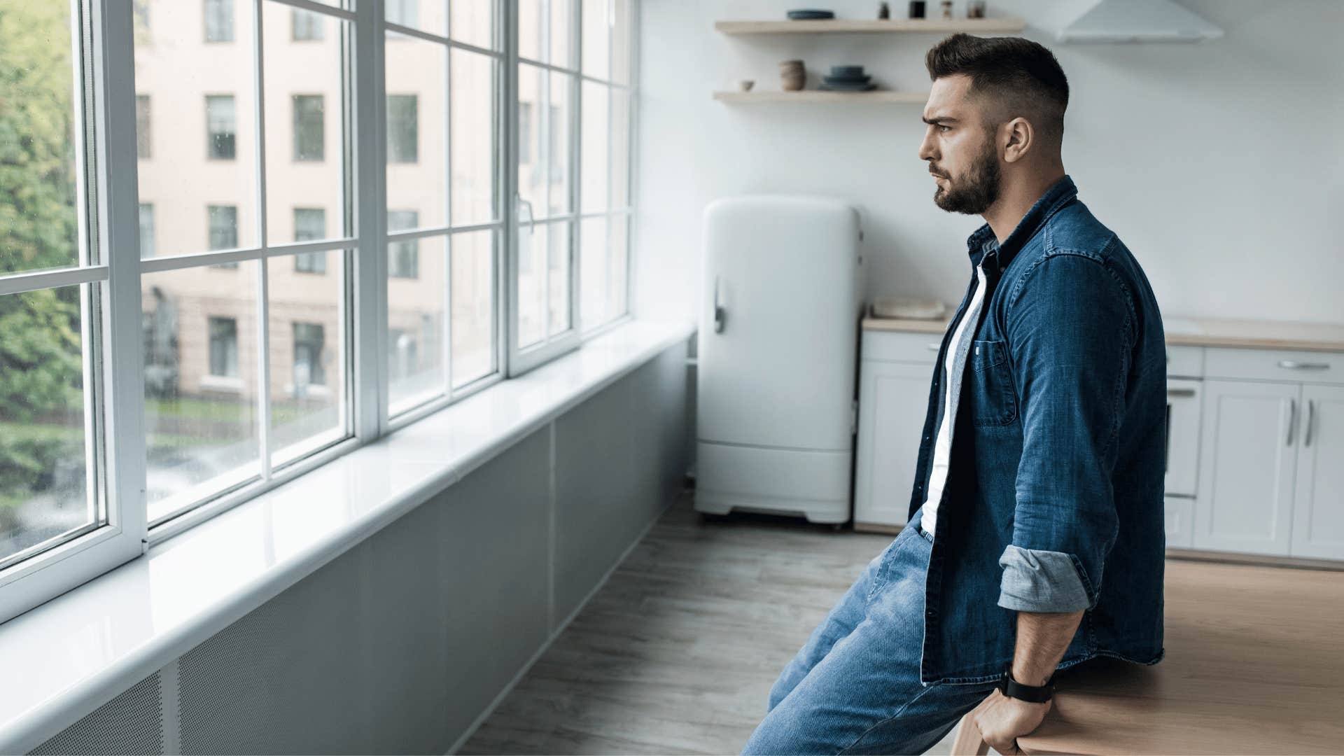 man in a minimalist room staring out of a window