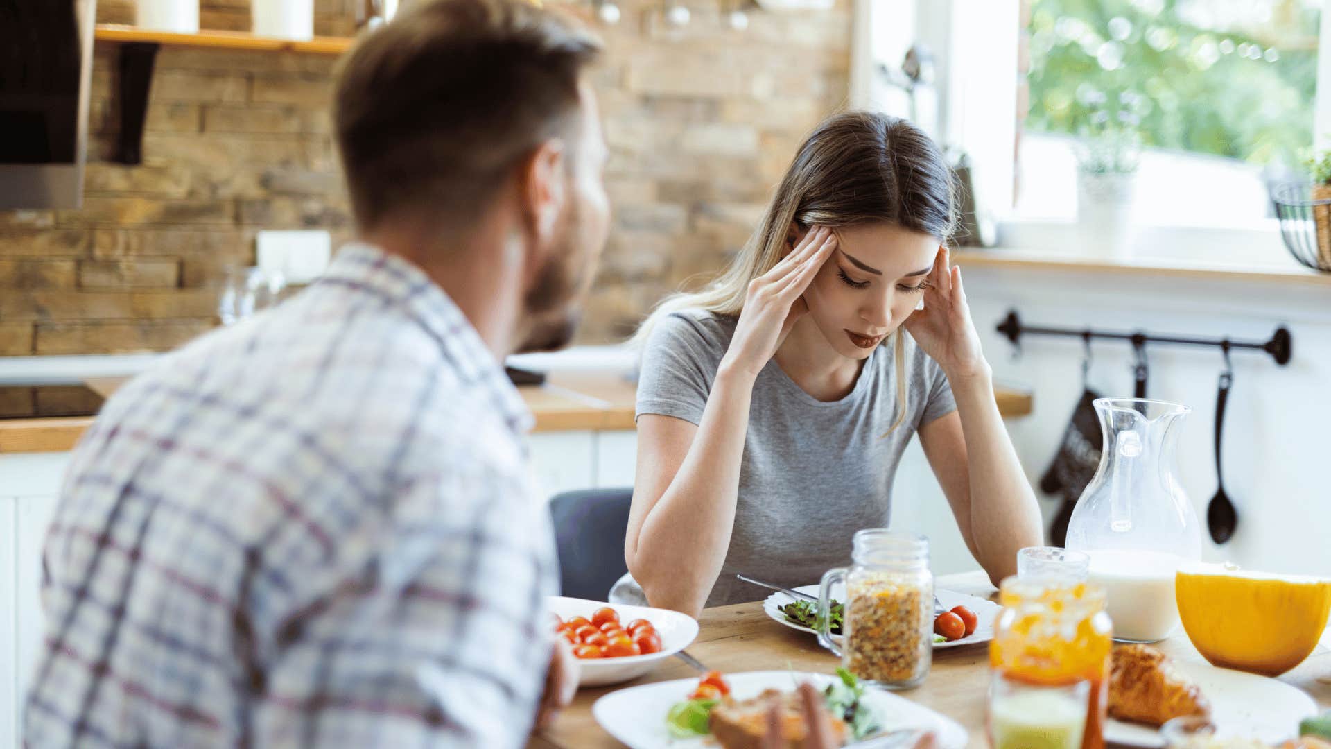 woman rubbing her temples having breakfast with man