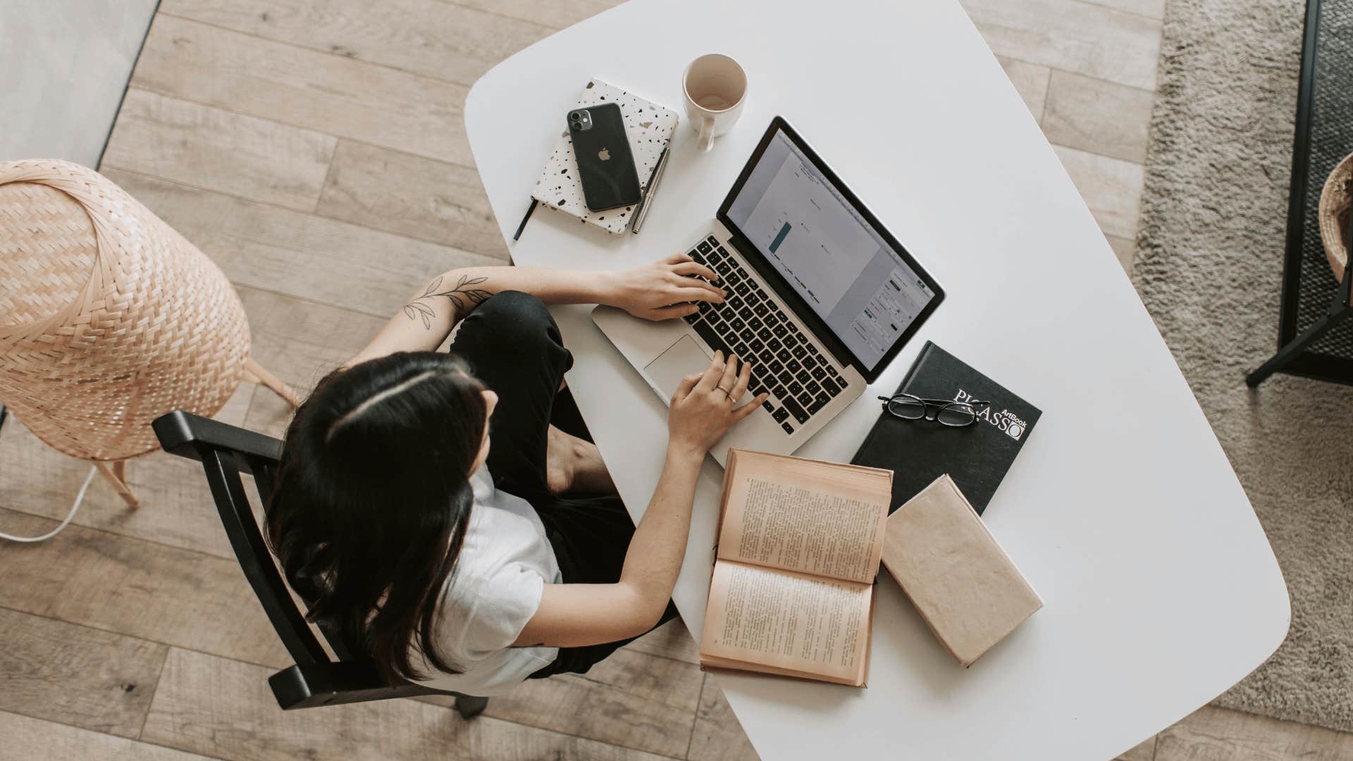 woman working on laptop with open book on desk