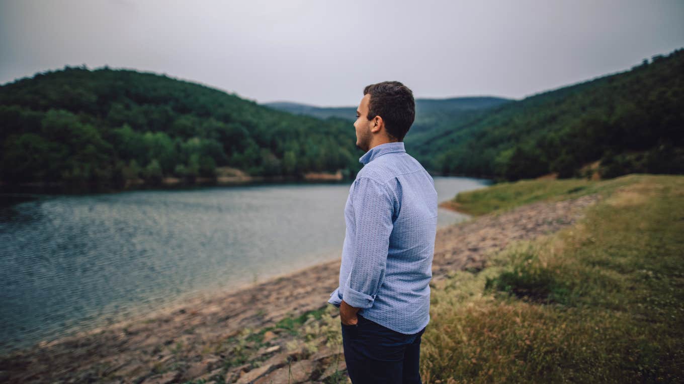 man stands alone admiring view of lake and mountains