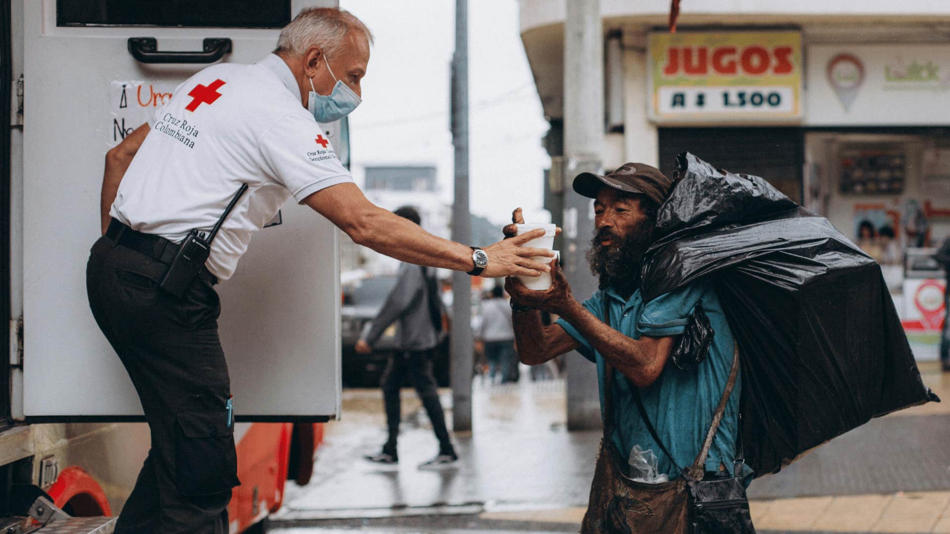 red cross man giving food and water to beggar