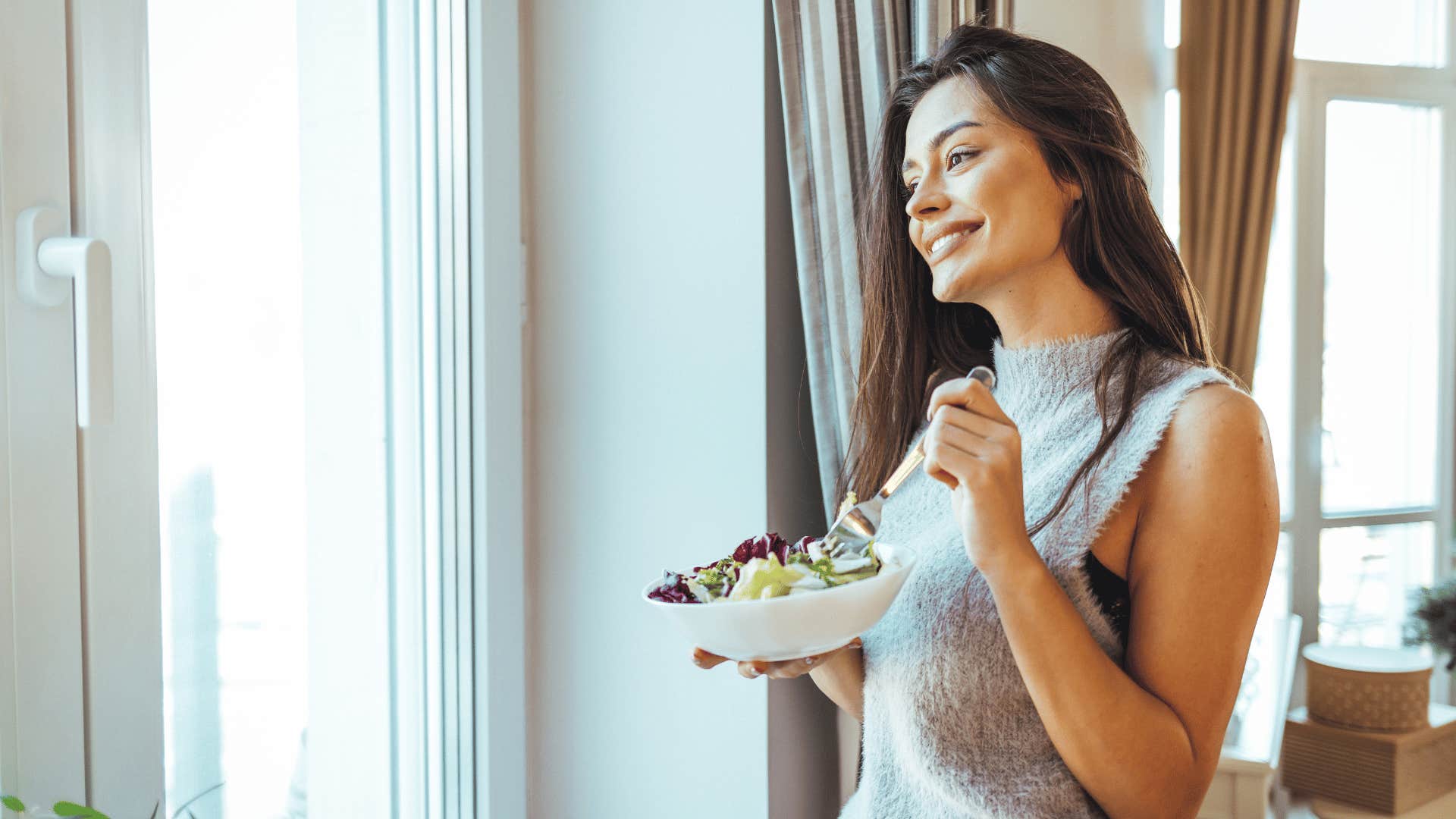 woman looking out of window while eating a healthy meal