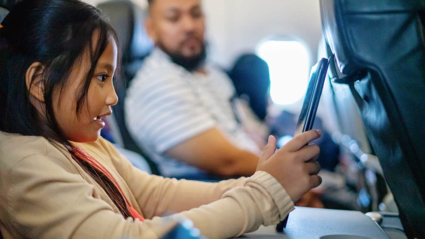 child using tablet on flight while passenger glances over