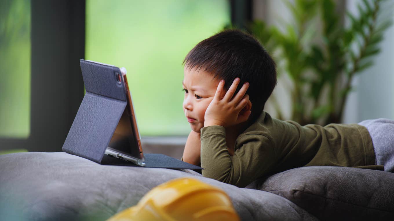 young child watching tablet screen sitting on couch at home