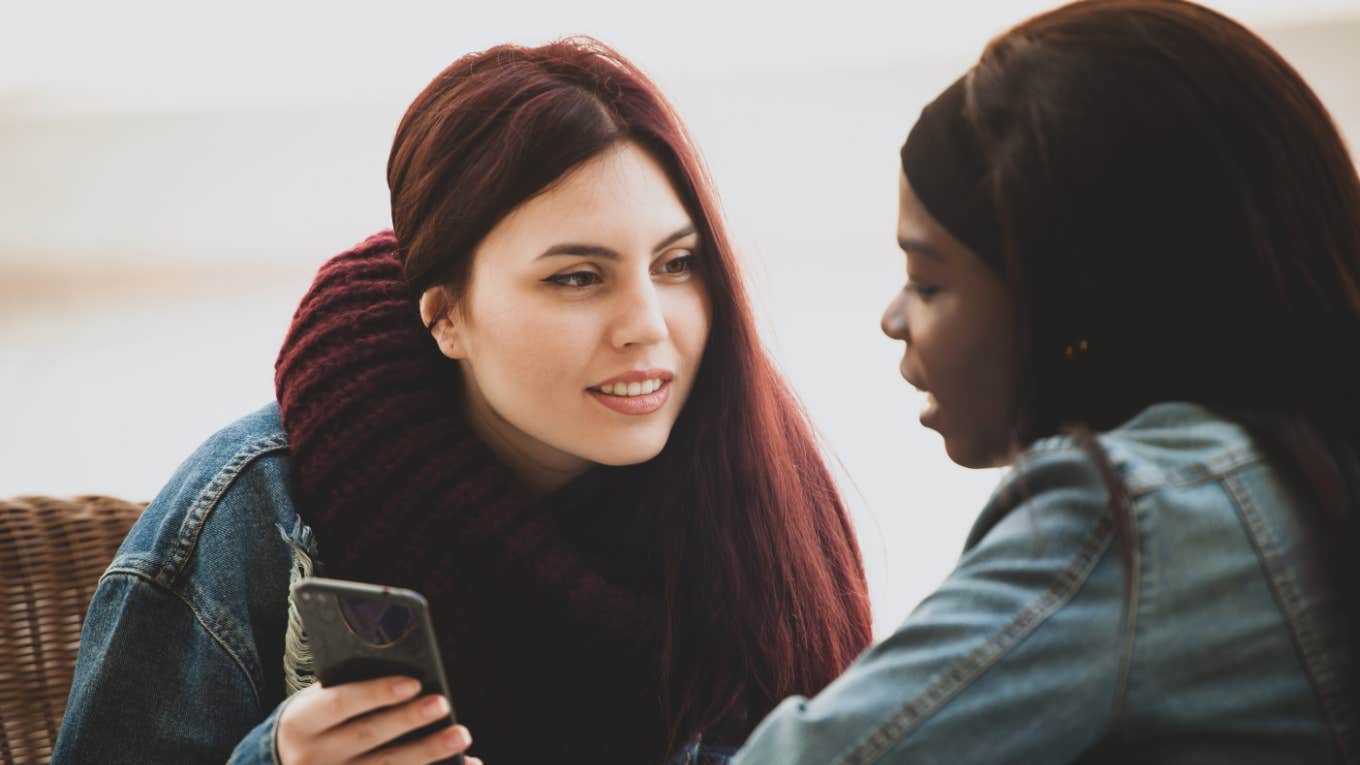 two female friends sitting together talking while holding phone